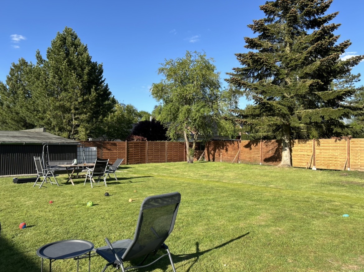Sonniger Garten von GOLDENDOGHOUSE mit Sitzgruppe und Hundespielzeug im Gras